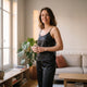 Femme portant l ensemble de nuit en satin noir dans son salon, debardeur a bretelles fines et pantalon long