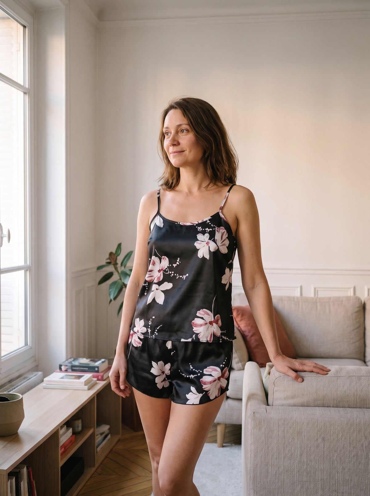 Ensemble pyjama en satin noir a fleurs, caraco et short, porte debout dans un salon