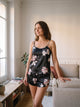 Ensemble pyjama en satin noir a fleurs, caraco et short, porte debout dans un salon