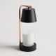 Lampe chauffe-bougie noire vue de face sur fond clair, un pot de bougie en verre posé au centre de son socle