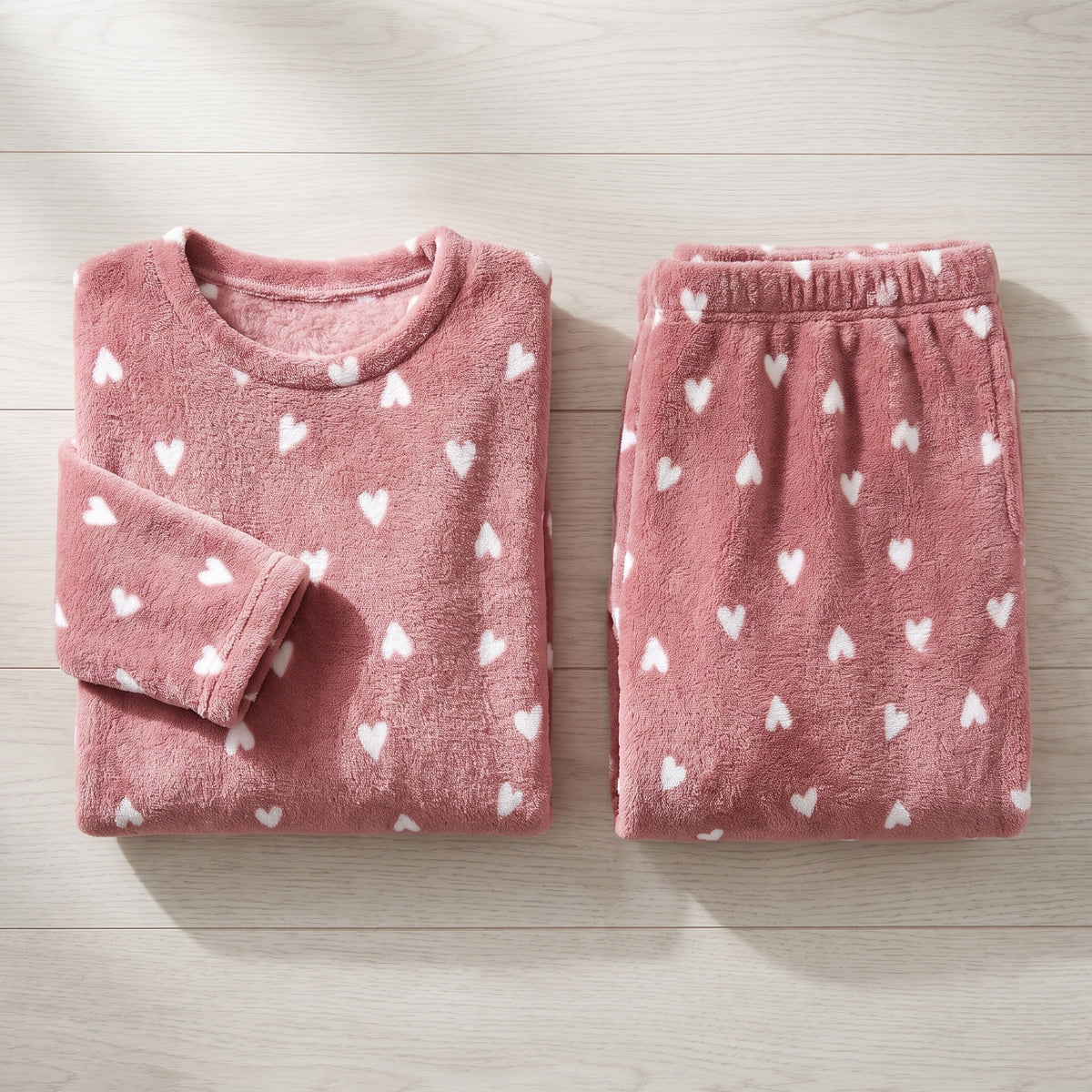 Haut et pantalon de pyjama polaire vieux rose pliés côte à côte sur un plan de bois clair