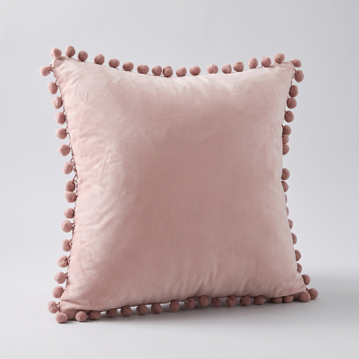 Housse de coussin en velours rose à pompons, vue de face sur fond neutre