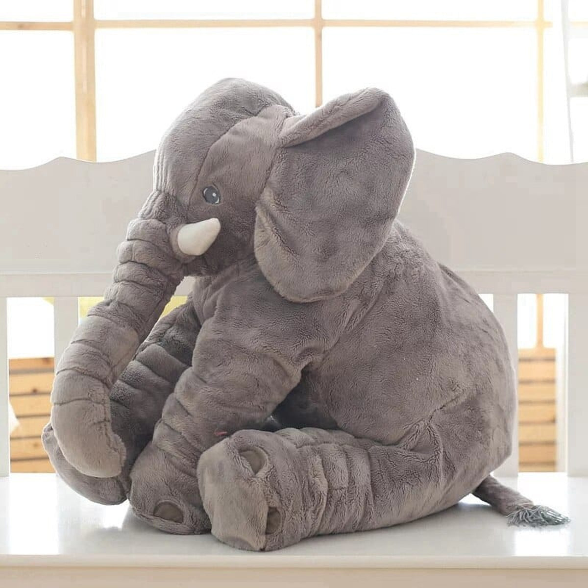 Peluche éléphant grise assise, grandes oreilles et trompe recourbée visibles