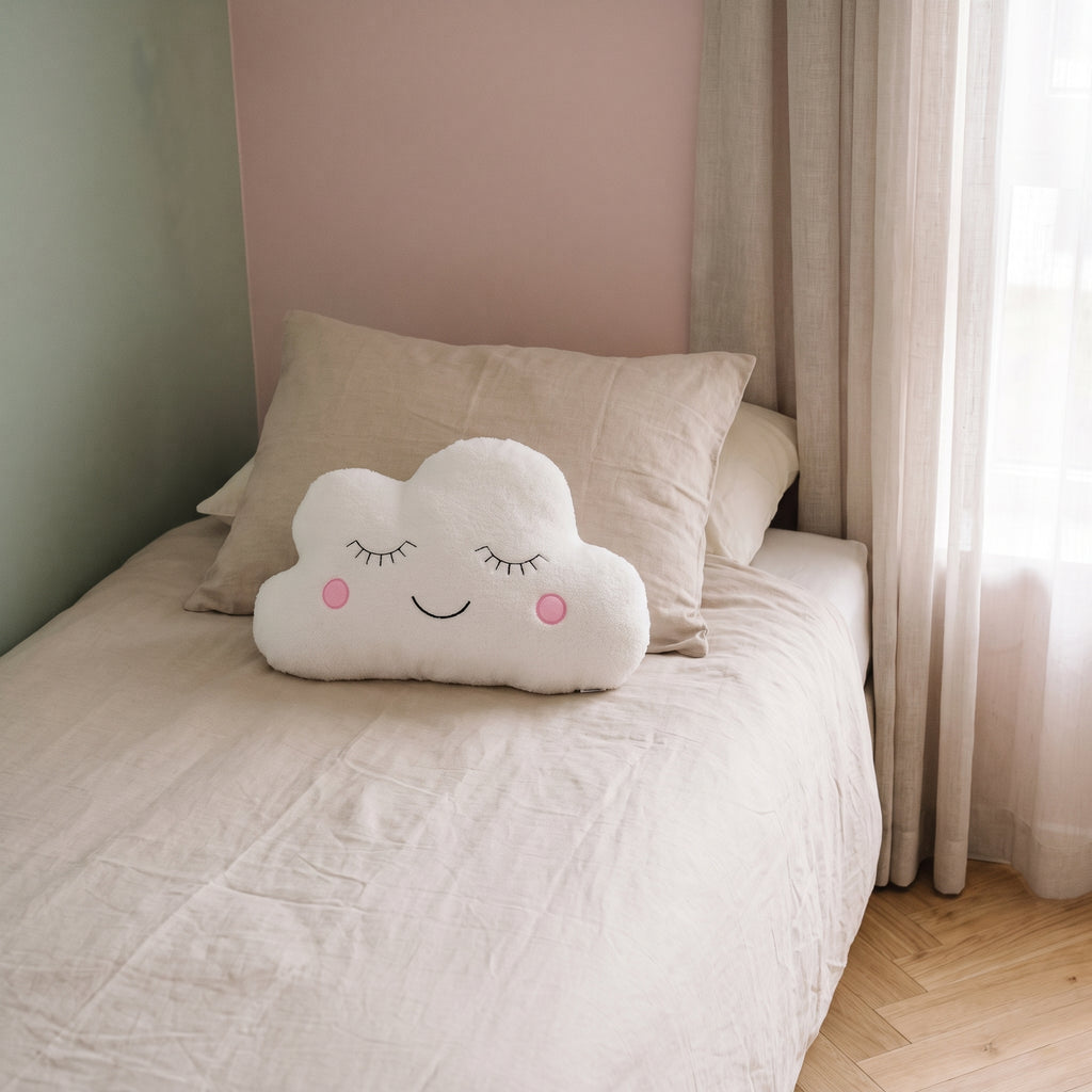 Peluche nuage blanche posée sur un lit dans une chambre d’enfant lumineuse aux murs pastel