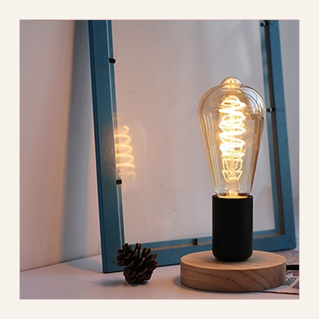 Lampe de table rétro modèle 5 à base noire et filament spiralé, allumée devant une fenêtre