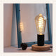 Lampe de table rétro modèle 5 à base noire et filament spiralé, allumée devant une fenêtre
