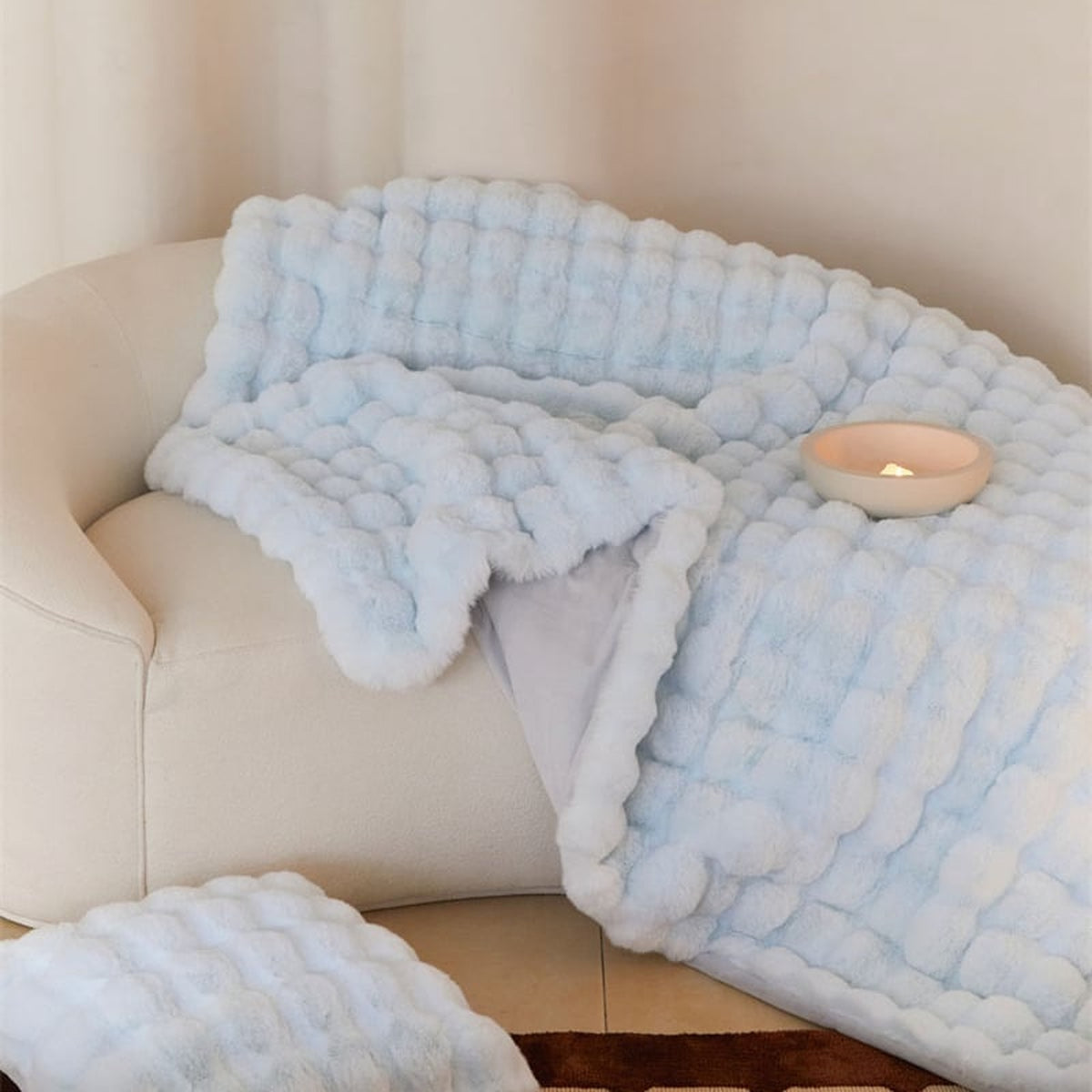 Plaid bleu très pâle imitation fourrure posé sur un canapé clair, avec ses rangées en relief et son revers visibles Image