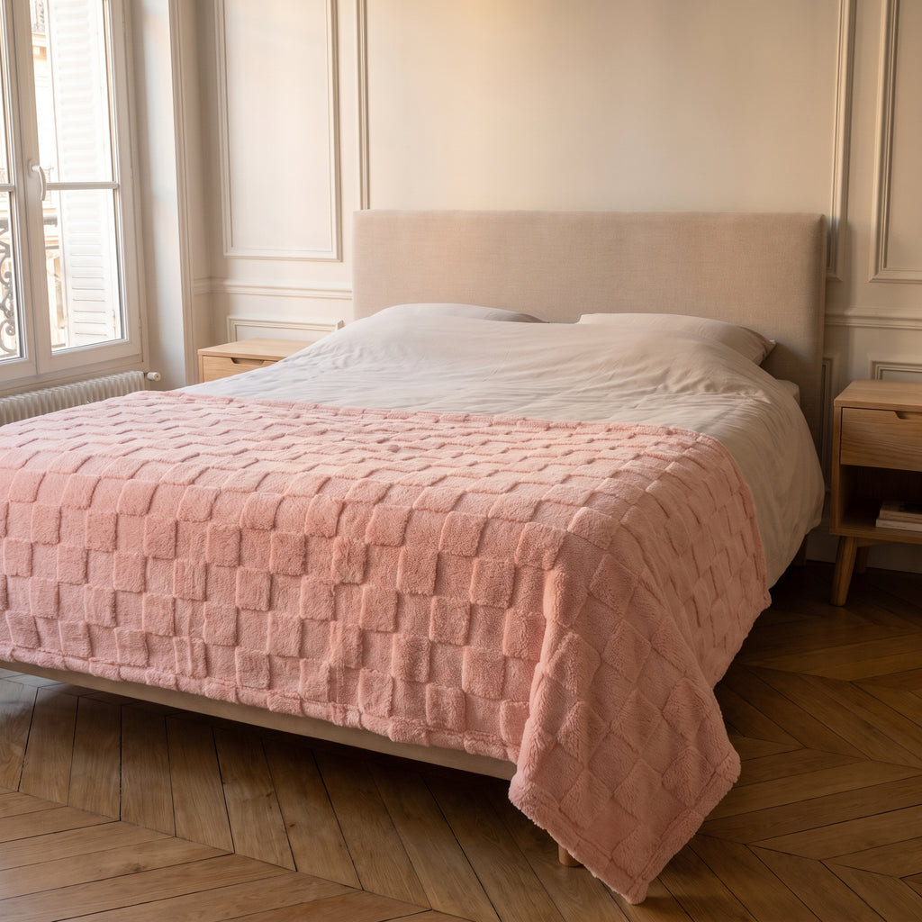 Plaid gaufré rose clair posé en travers du pied du lit