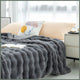 Plaid gris imitation fourrure déployé sur un lit, avec ses rangées en relief visibles