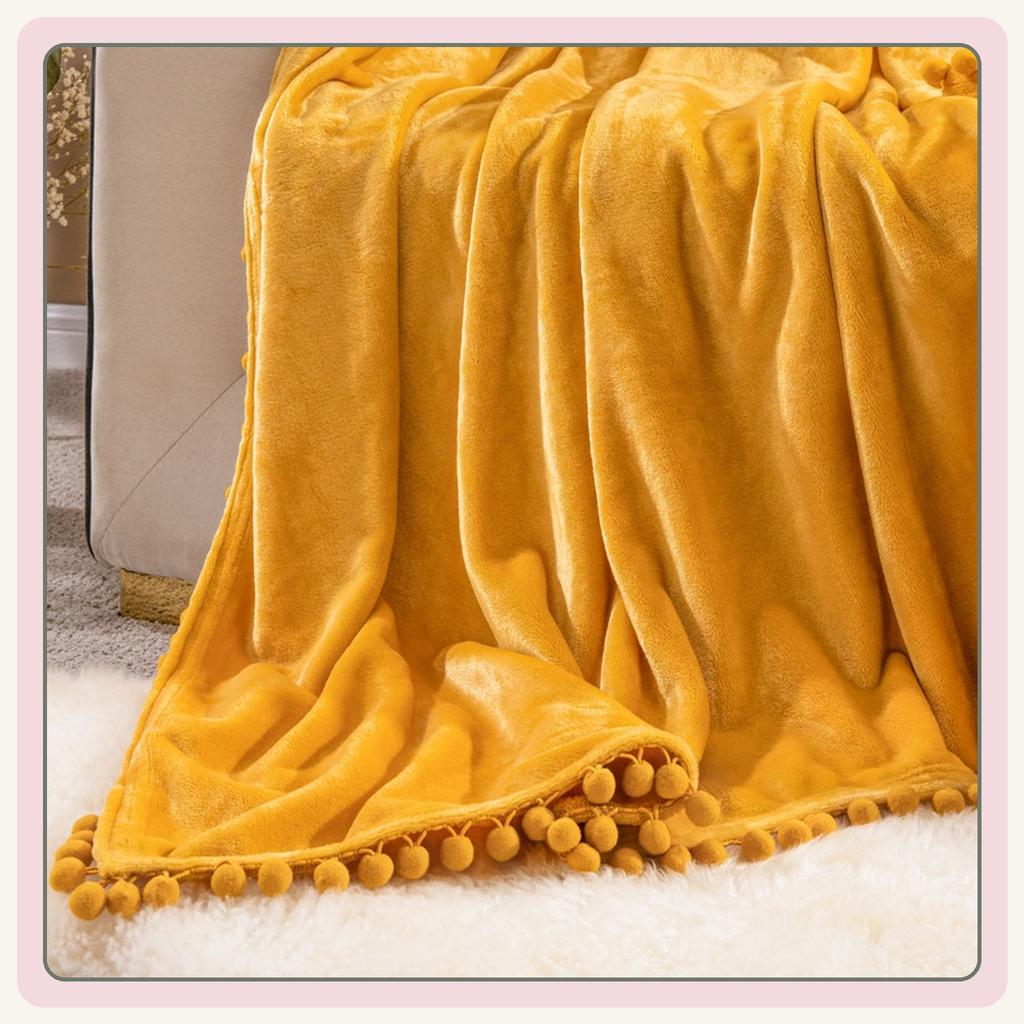 Plaid molletonné jaune à pompons déployé sur un canapé