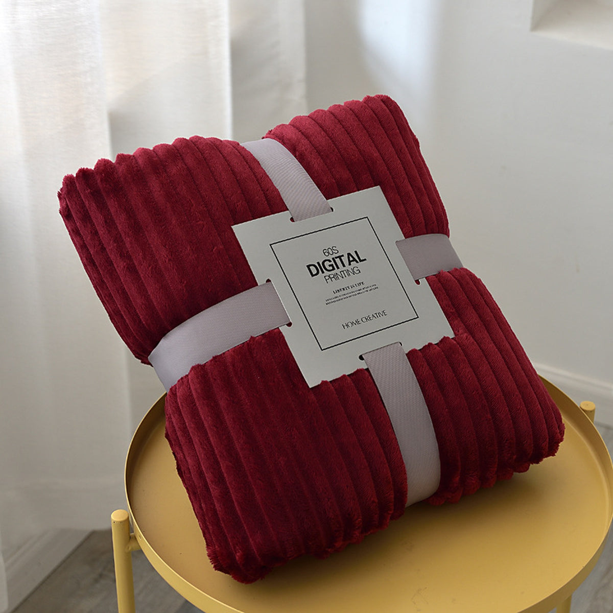 Plaid polaire bordeaux plié, ses côtes en relief et son emballage visibles