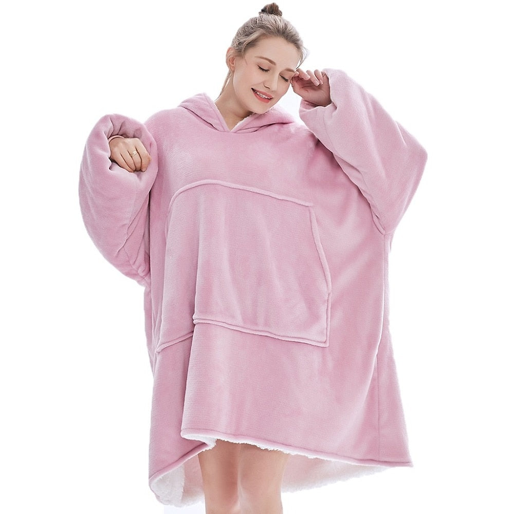 Le plaid à capuche rose clair porté de face, un bras levé qui déploie la manche, la doublure sherpa crème visible sur tout le bord bas arrondi