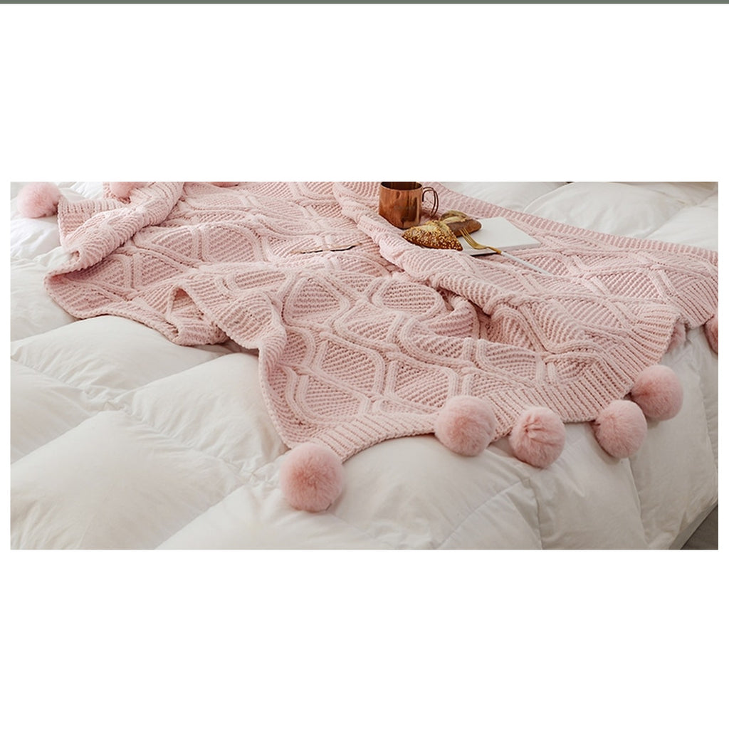 Plaid tricoté rose à pompons déployé sur un lit clair