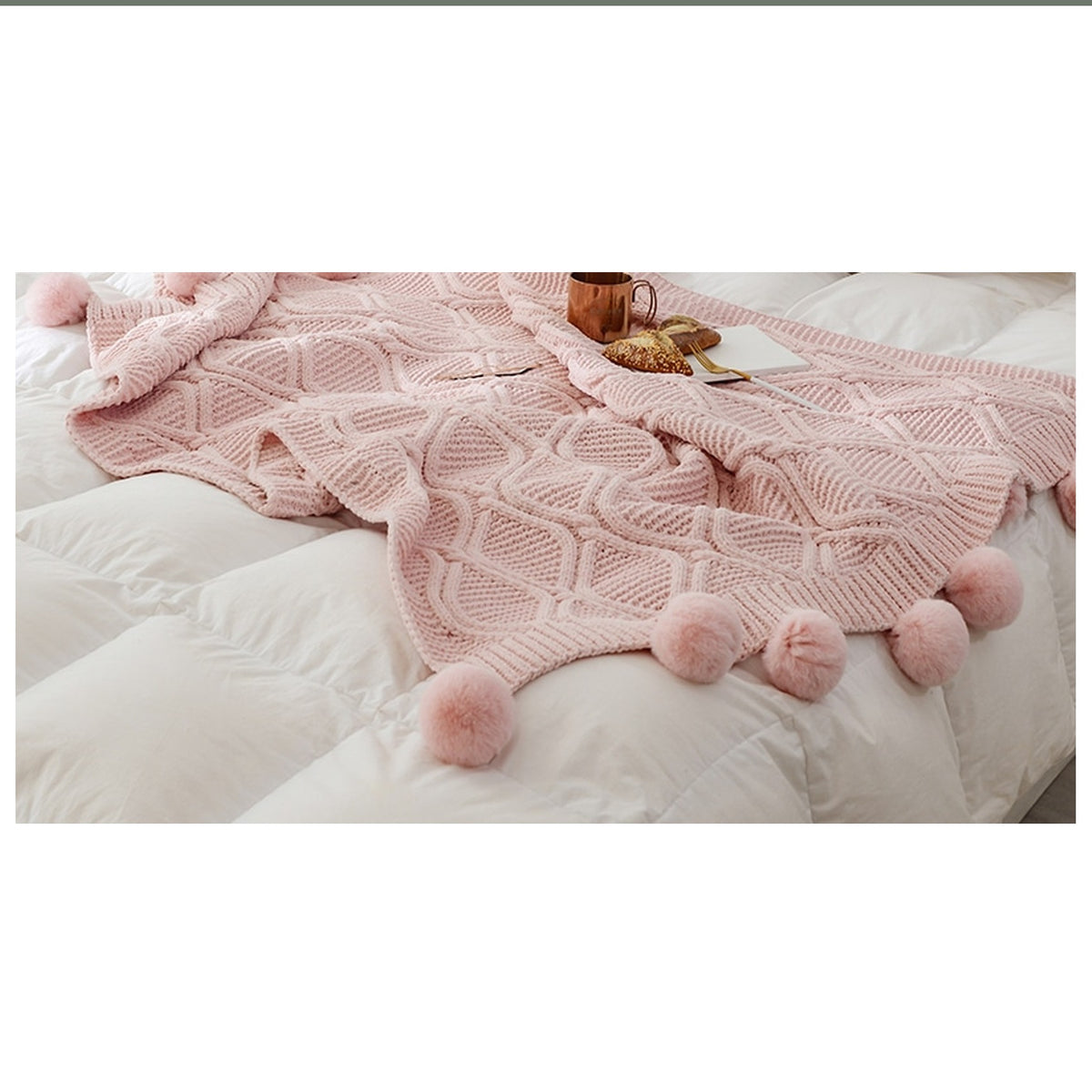 Plaid tricoté rose à pompons déployé sur un lit clair