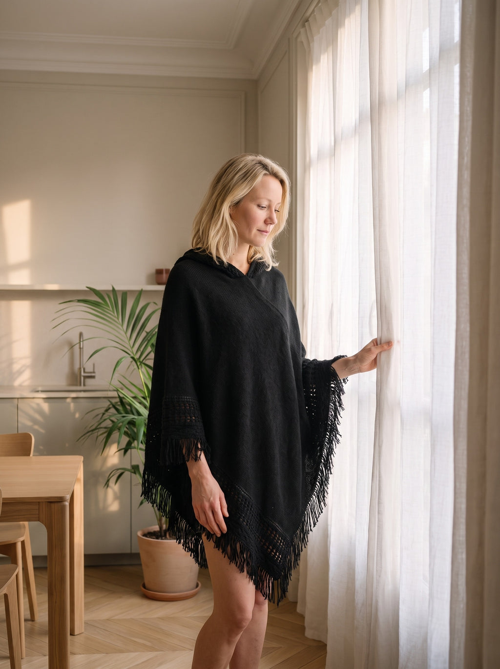Femme du casting portant le poncho noir à franges près de la fenêtre du coin repas