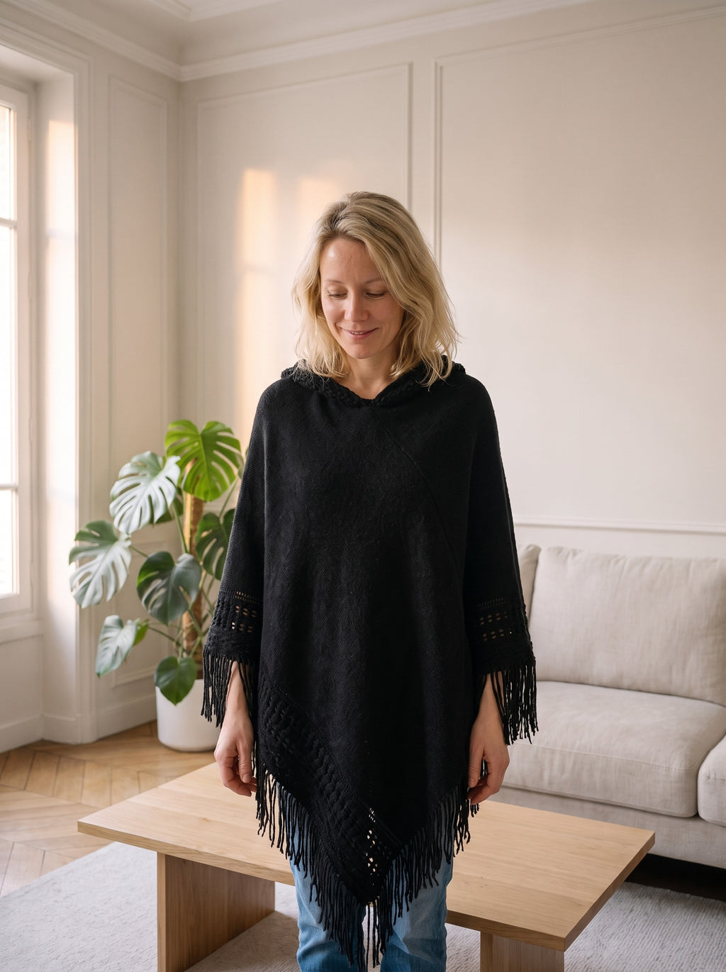 Femme du casting portant le poncho noir à capuche et franges dans son salon