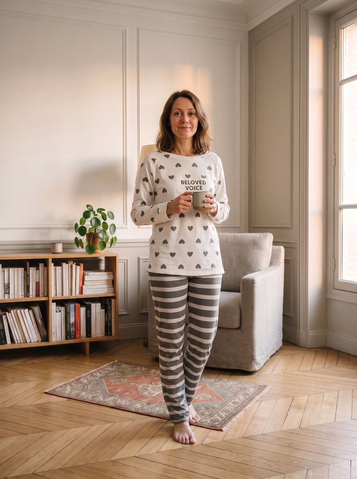 Ensemble pyjama blanc a petits coeurs gris porte debout au coin lecture, avec son pantalon raye gris et blanc.