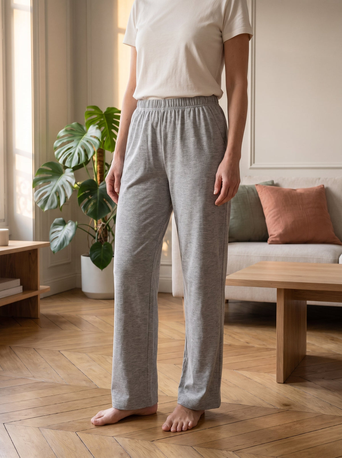 Bas de pyjama gris chine porte debout pres de la fenetre, vue de la ceinture aux pieds nus.