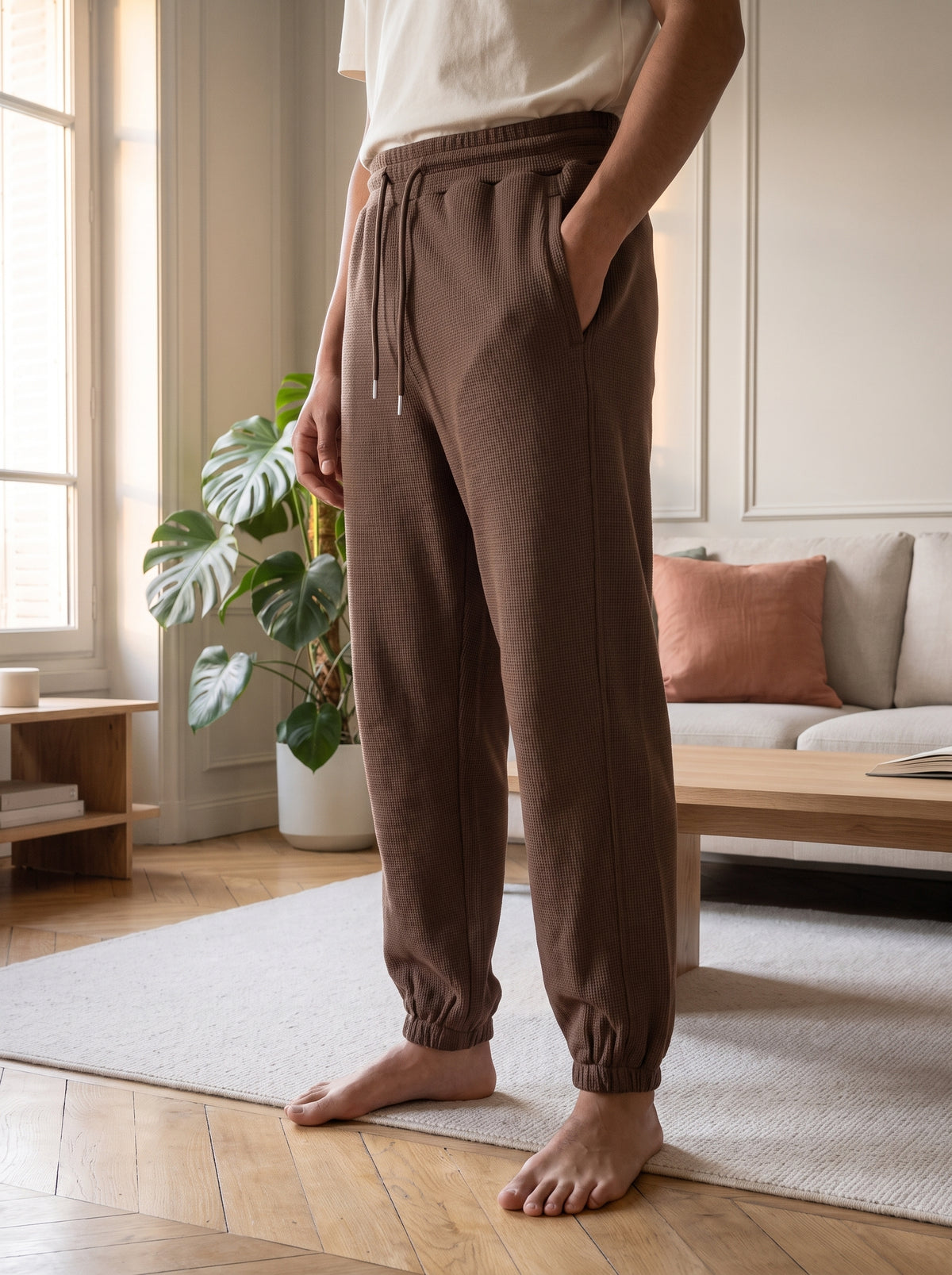 Pantalon de jogging gaufre marron porte, debout dans un salon, pieds nus sur le tapis