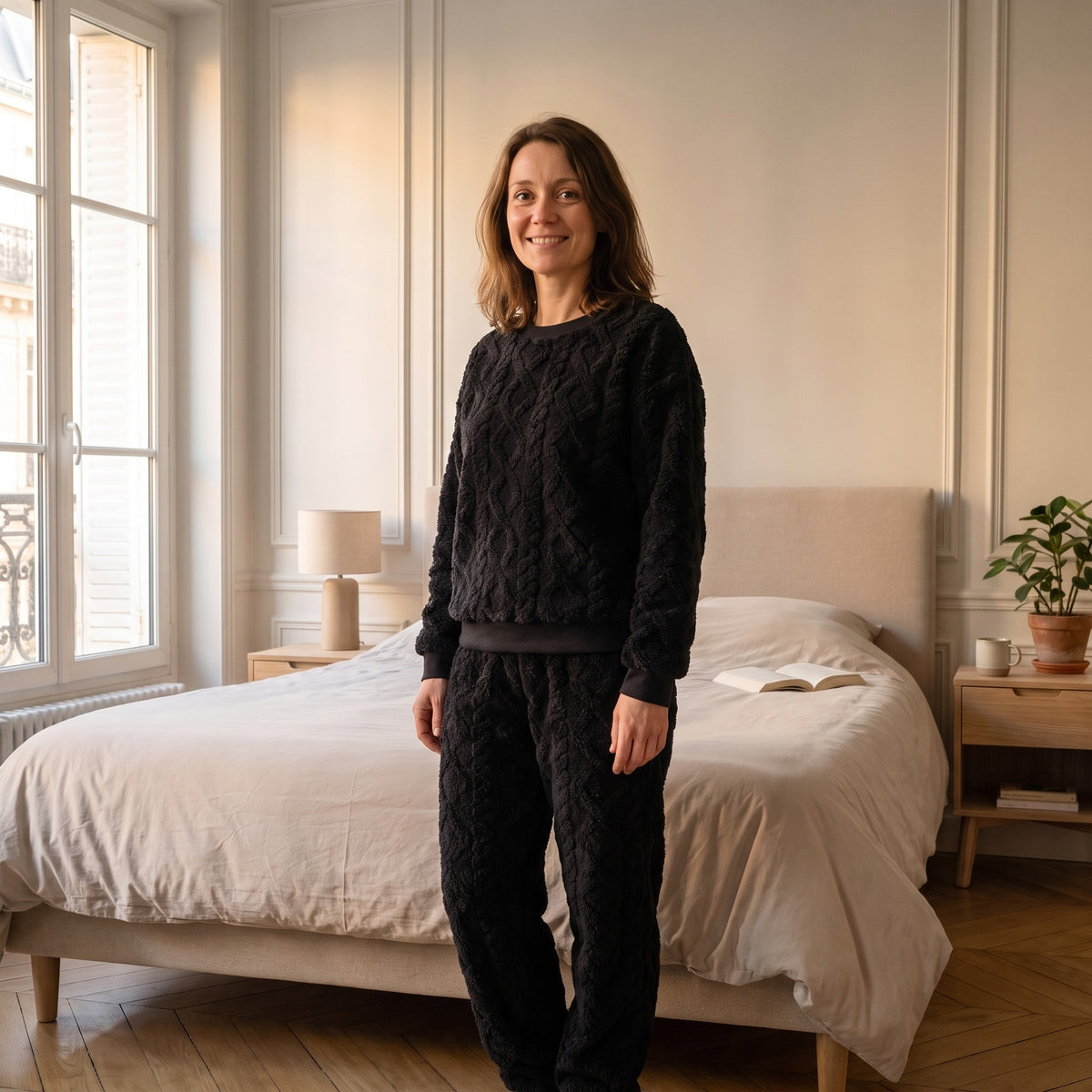 Femme portant l'ensemble pyjama noir en coton effet tricot, debout dans sa chambre