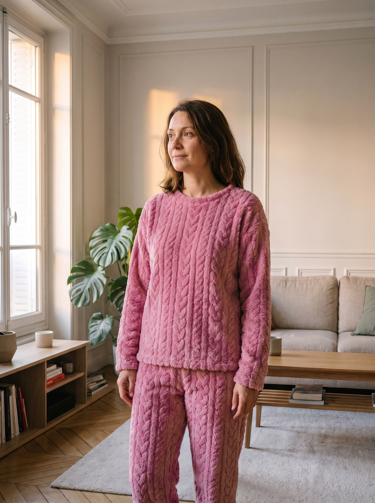 Pyjama femme en velours polaire rose à torsades, porté de trois quarts dans le salon, le regard vers la fenêtre