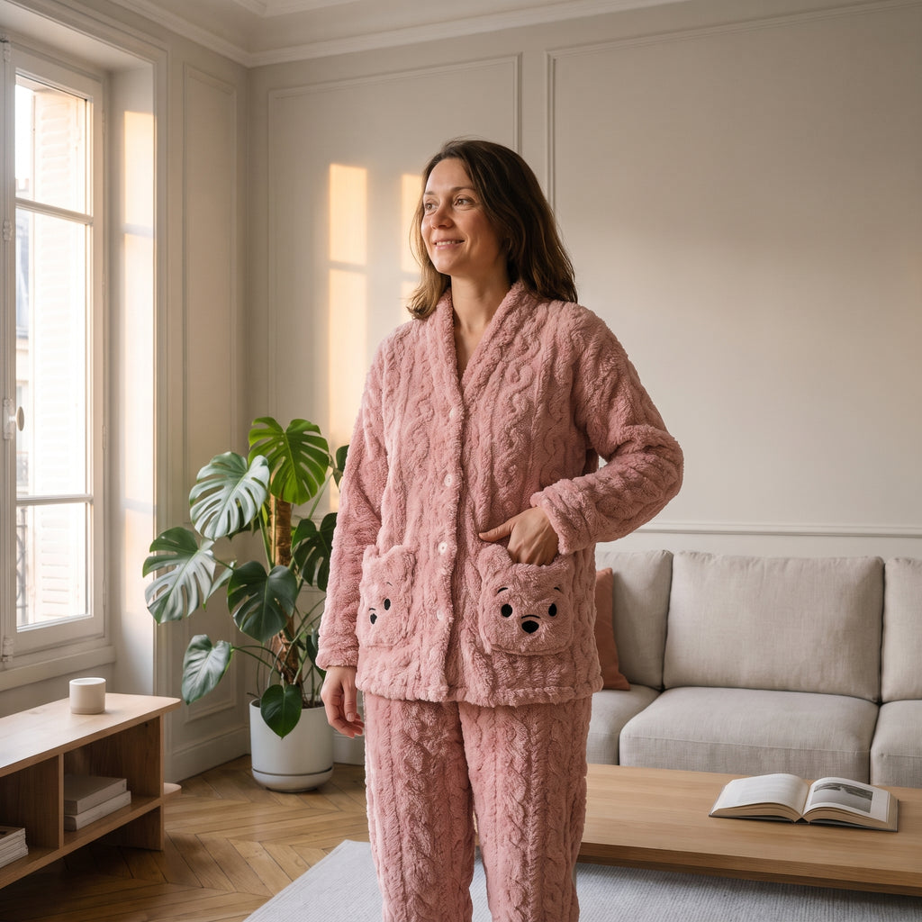 Femme en pyjama en peluche ourson rose, debout dans un salon, une main posée sur la poche ourson