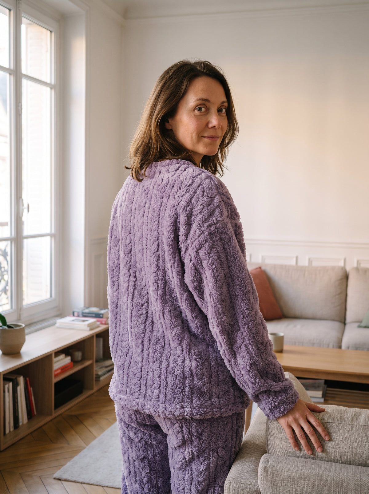 Pyjama femme en velours polaire violet a torsades, porte de trois quarts pres du canape