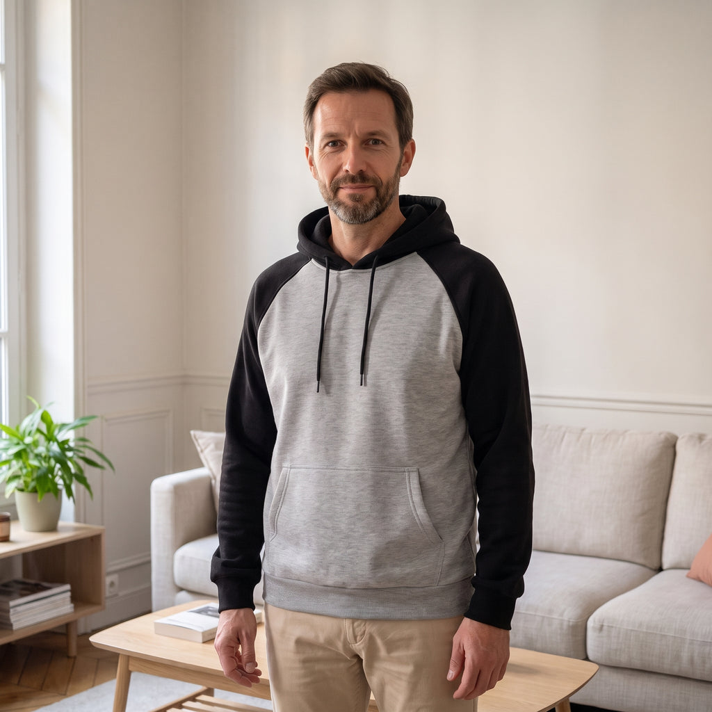 Sweat homme bicolore à manches raglan, gris et noir, porté dans un salon