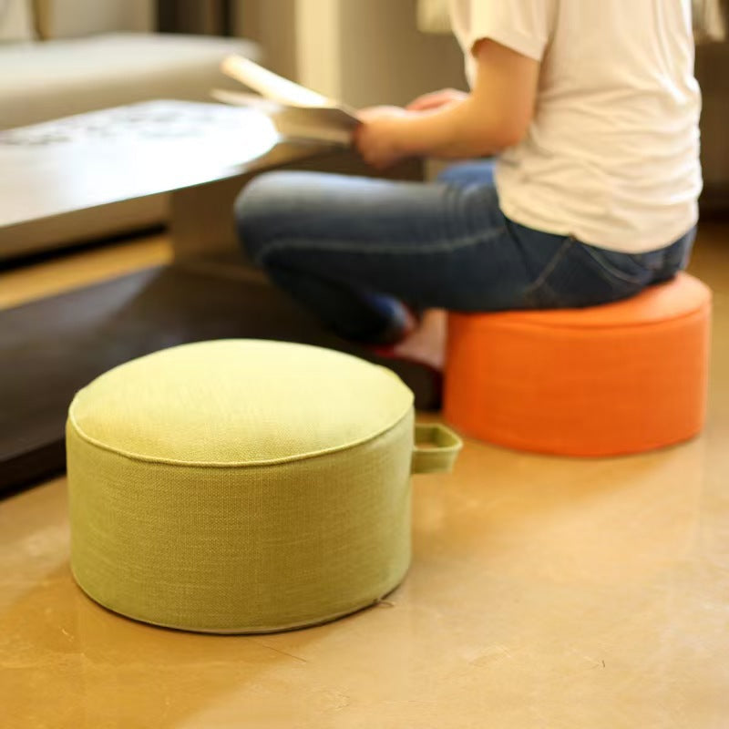 Deux poufs de sol en lin, vert et orange, à côté d'une personne assise près d'une table basse