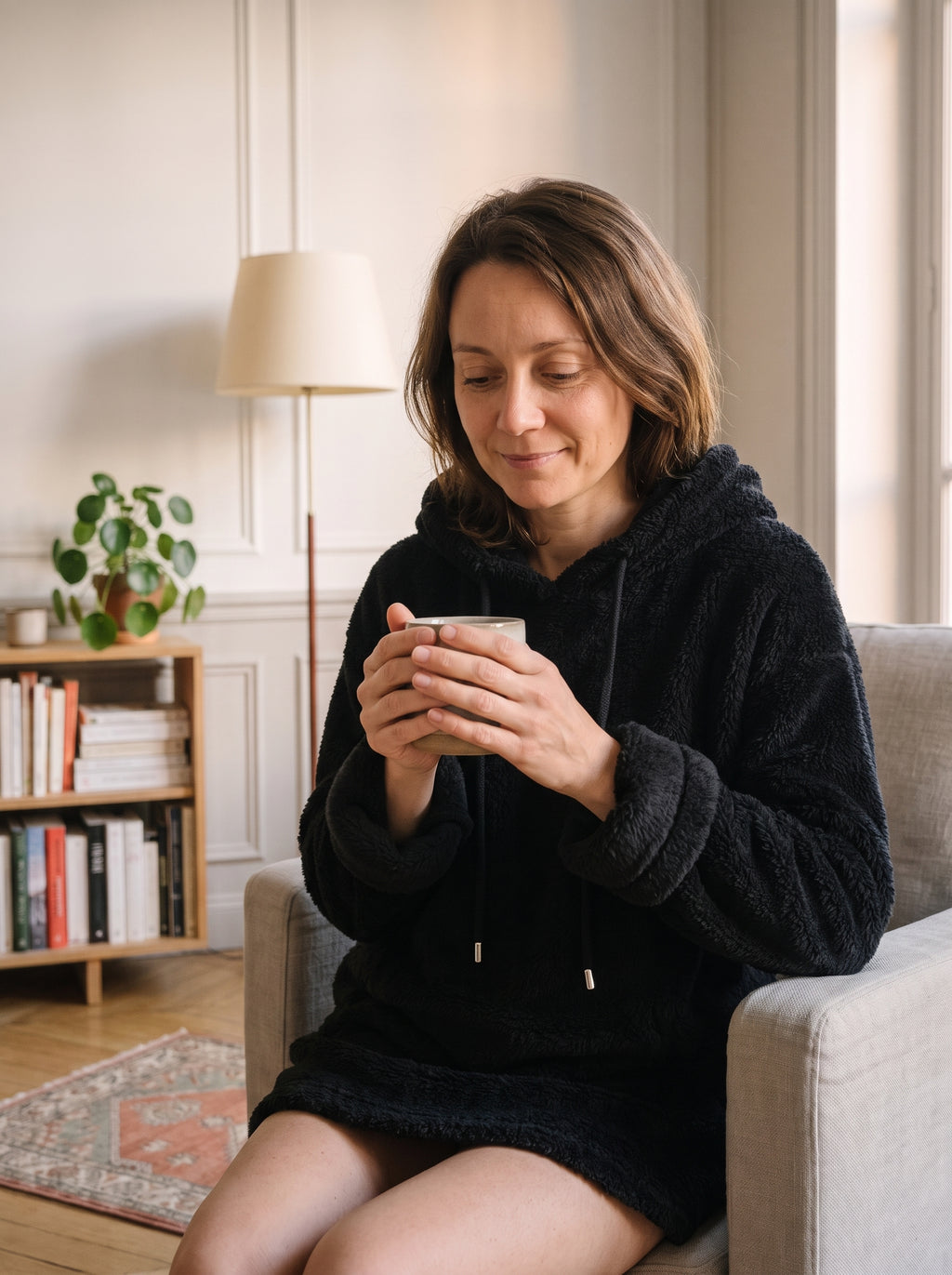 Femme du casting portant le pull long à capuche peluche noir dans le coin lecture