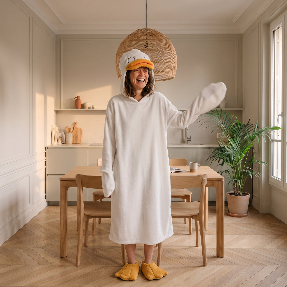 Femme qui rit en pyjama canard dans un coin repas, capuche relevée et bec orange en avant Image