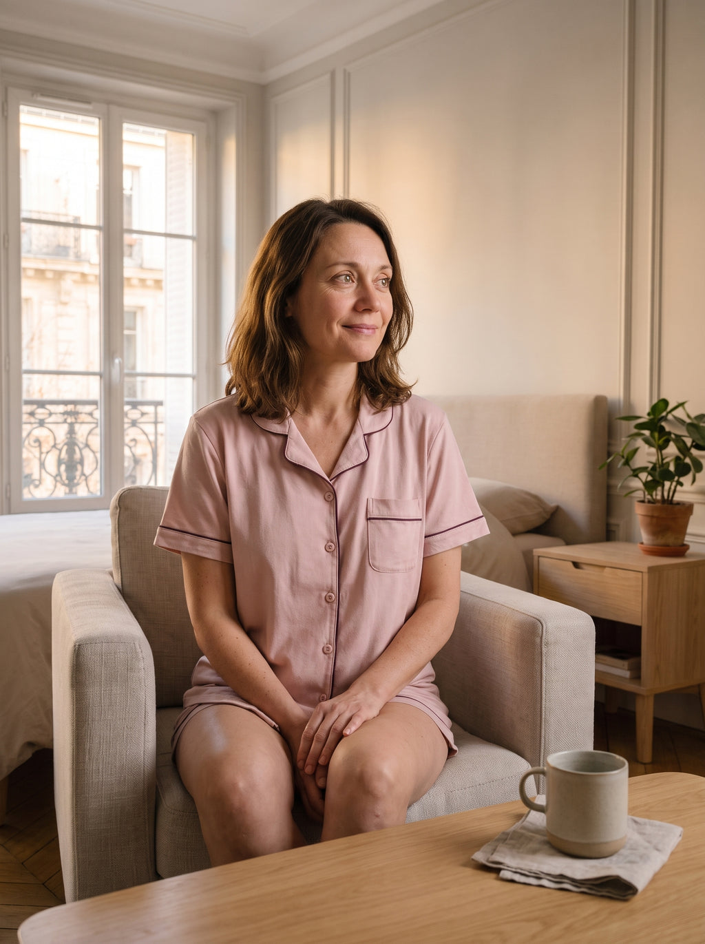 Femme du casting en pyjama d’été rose assise dans une chambre lumineuse.