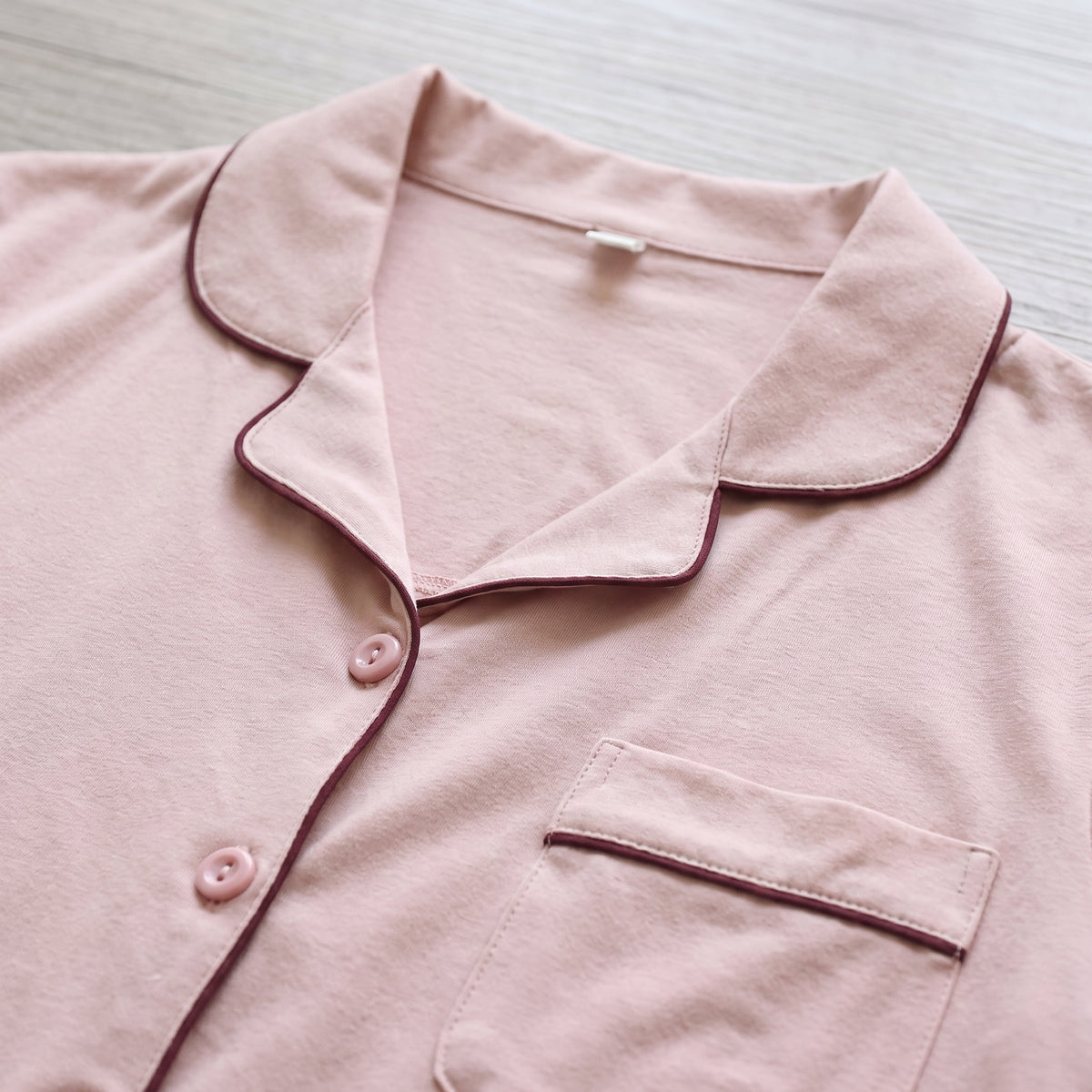 Vue rapprochée du col, des boutons et du passepoil du pyjama rose poudré.