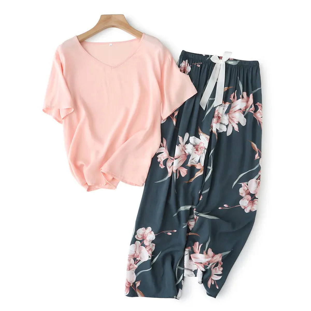 Pyjama deux pièces femme. Haut rose poudré et pantalon large marine à magnolias, posés à plat sur un cintre.