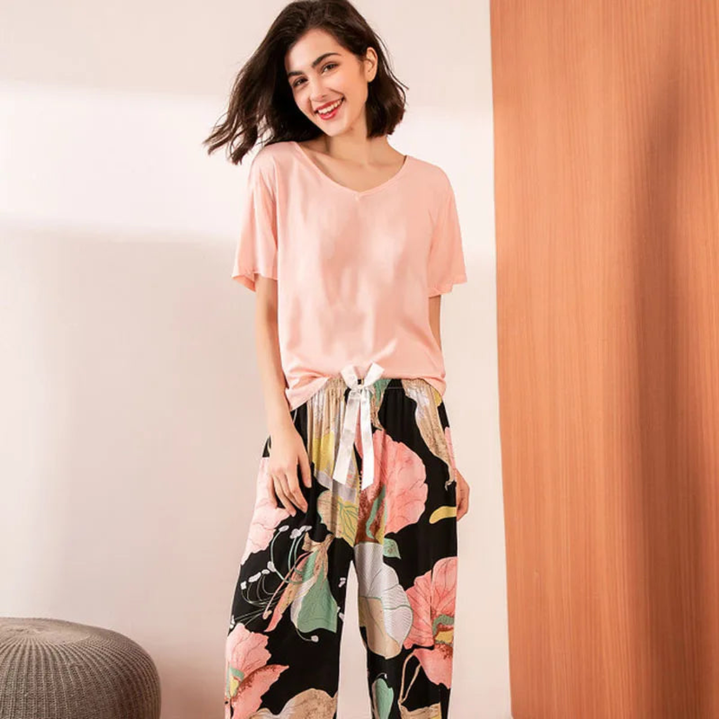 Pyjama deux pièces femme. Haut rose poudré et pantalon large noir à grandes fleurs, portés debout de face.