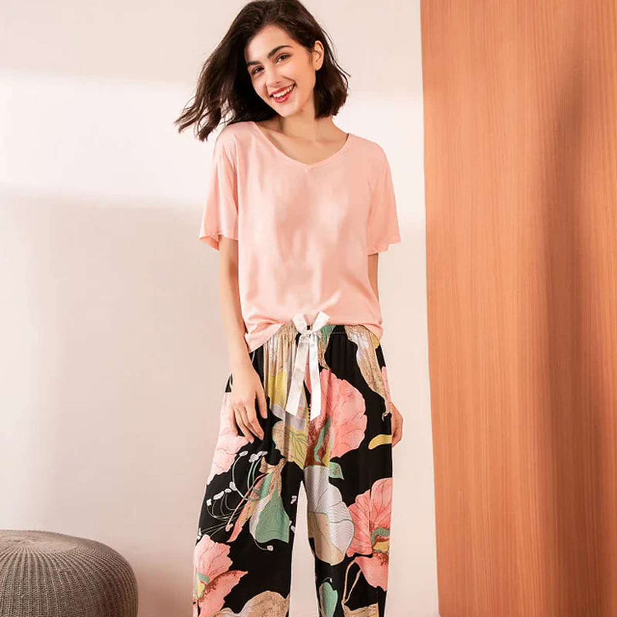 Pyjama deux pièces femme. Haut rose poudré et pantalon large noir à grandes fleurs, portés debout de face.
