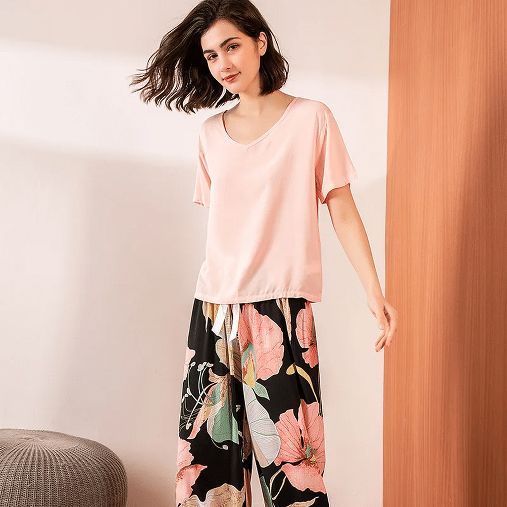Pyjama femme, haut rose et pantalon large grandes fleurs noir, debout, le bras tendu sur le côté.