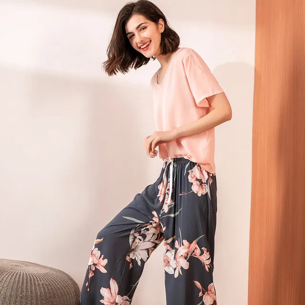 Pyjama femme, haut rose et pantalon large lys roses ardoise, portés debout devant un mur clair.