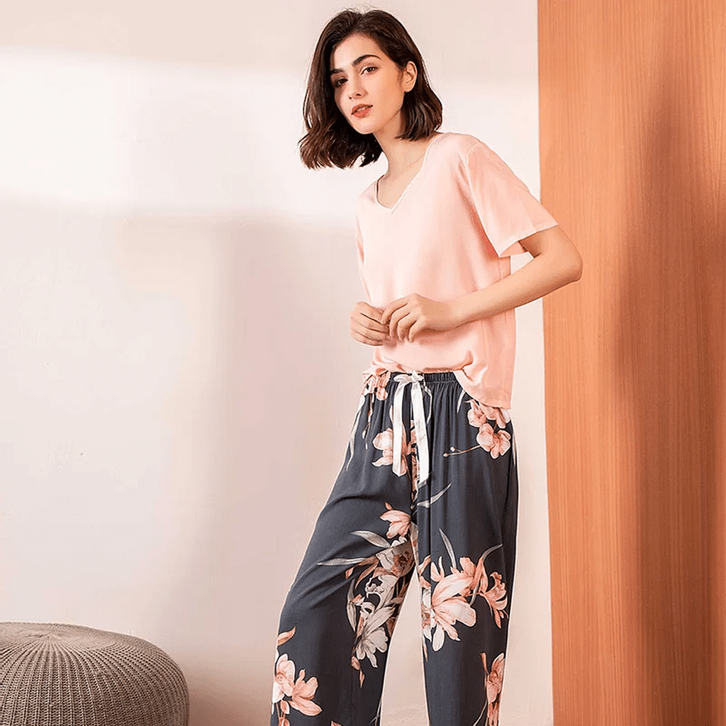 Pyjama femme, haut rose et pantalon large magnolias ardoise, portés debout devant un mur clair.