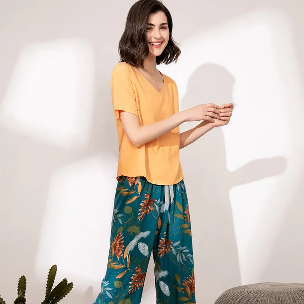 Pyjama femme, haut abricot et pantalon large feuillage bleu canard, portés debout devant un mur clair.