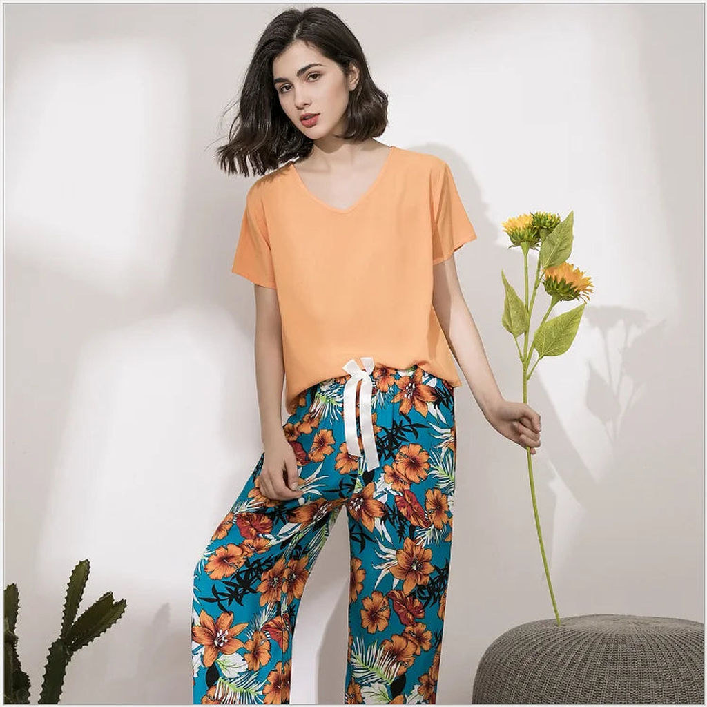 Pyjama femme, haut abricot et pantalon large hibiscus turquoise, portés debout devant un mur clair.