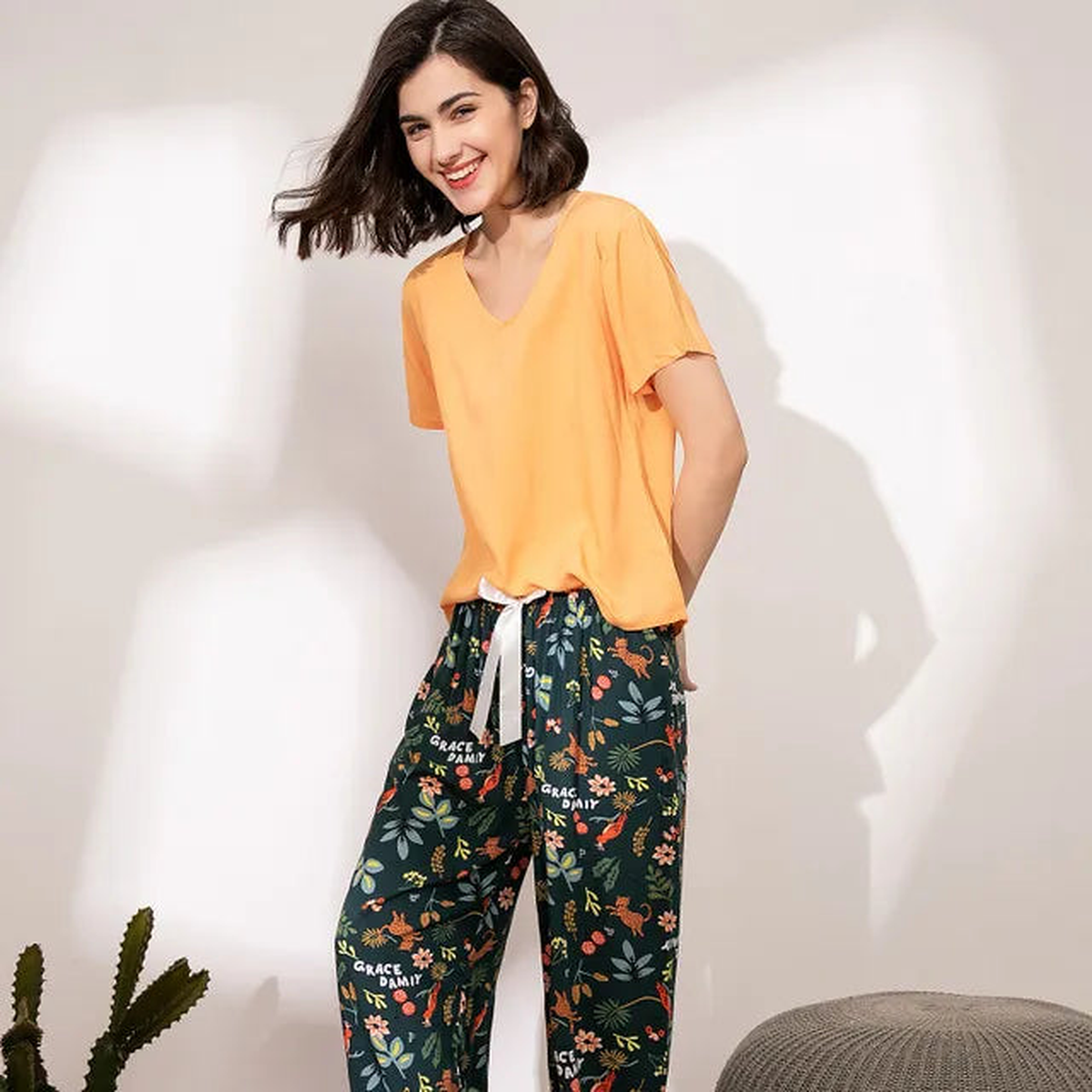 Pyjama femme, haut abricot et pantalon large jardin vert forêt, portés debout devant un mur clair.