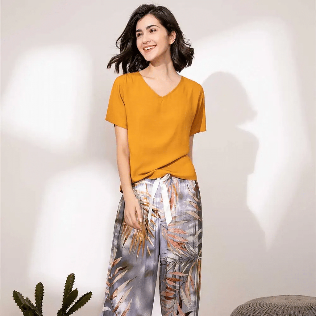 Pyjama femme, haut safran et pantalon large palmes grises, debout de trois quarts, le regard de côté.