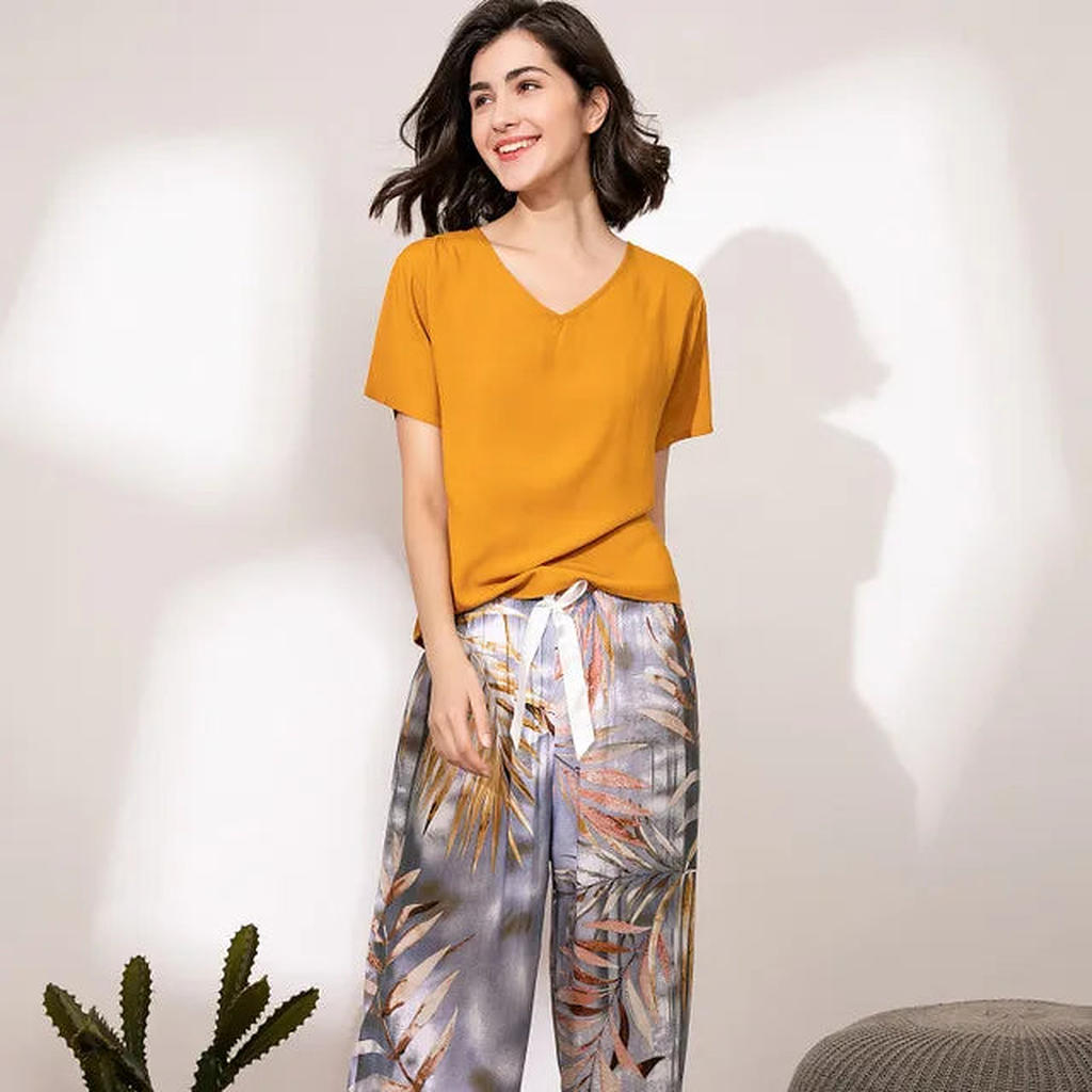 Pyjama femme, haut safran et pantalon large palmes grises, debout de face devant un mur clair.
