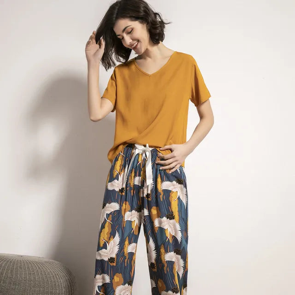 Pyjama femme, haut moutarde et pantalon large grues marine, portés debout devant un mur clair.
