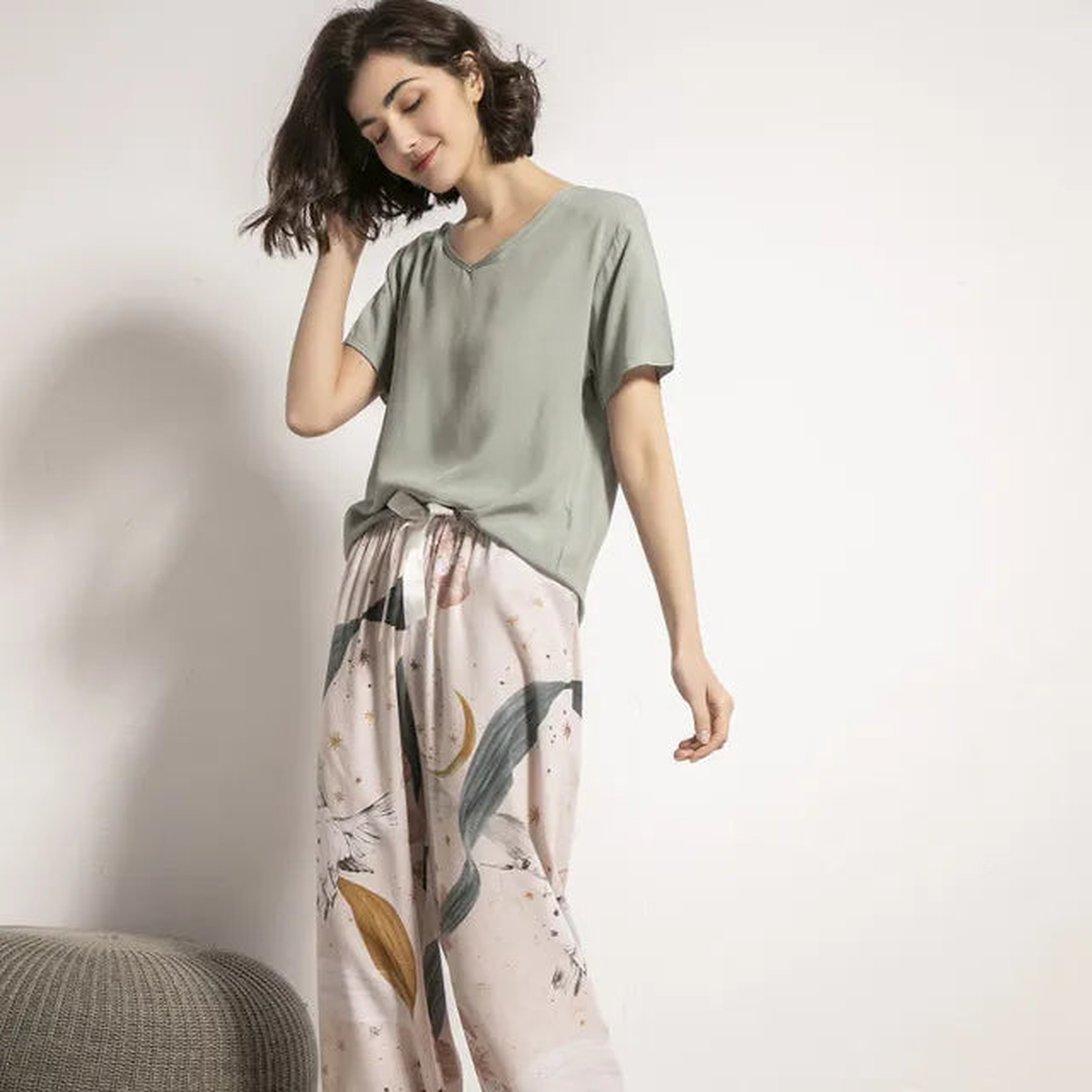 Pyjama femme, haut sauge et pantalon large feuillage écru, portés debout devant un mur clair.