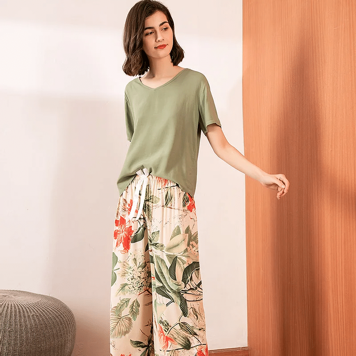 Pyjama femme, haut kaki et pantalon large feuillage écru, portés debout devant un mur clair.