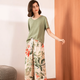 Pyjama femme, haut kaki et pantalon large feuillage écru, portés debout devant un mur clair.