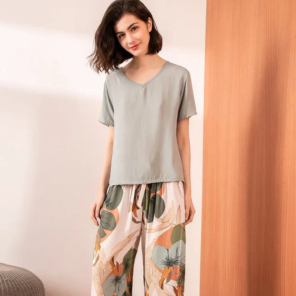 Pyjama femme, haut gris perle et pantalon large feuillage rose, portés debout devant un mur clair.