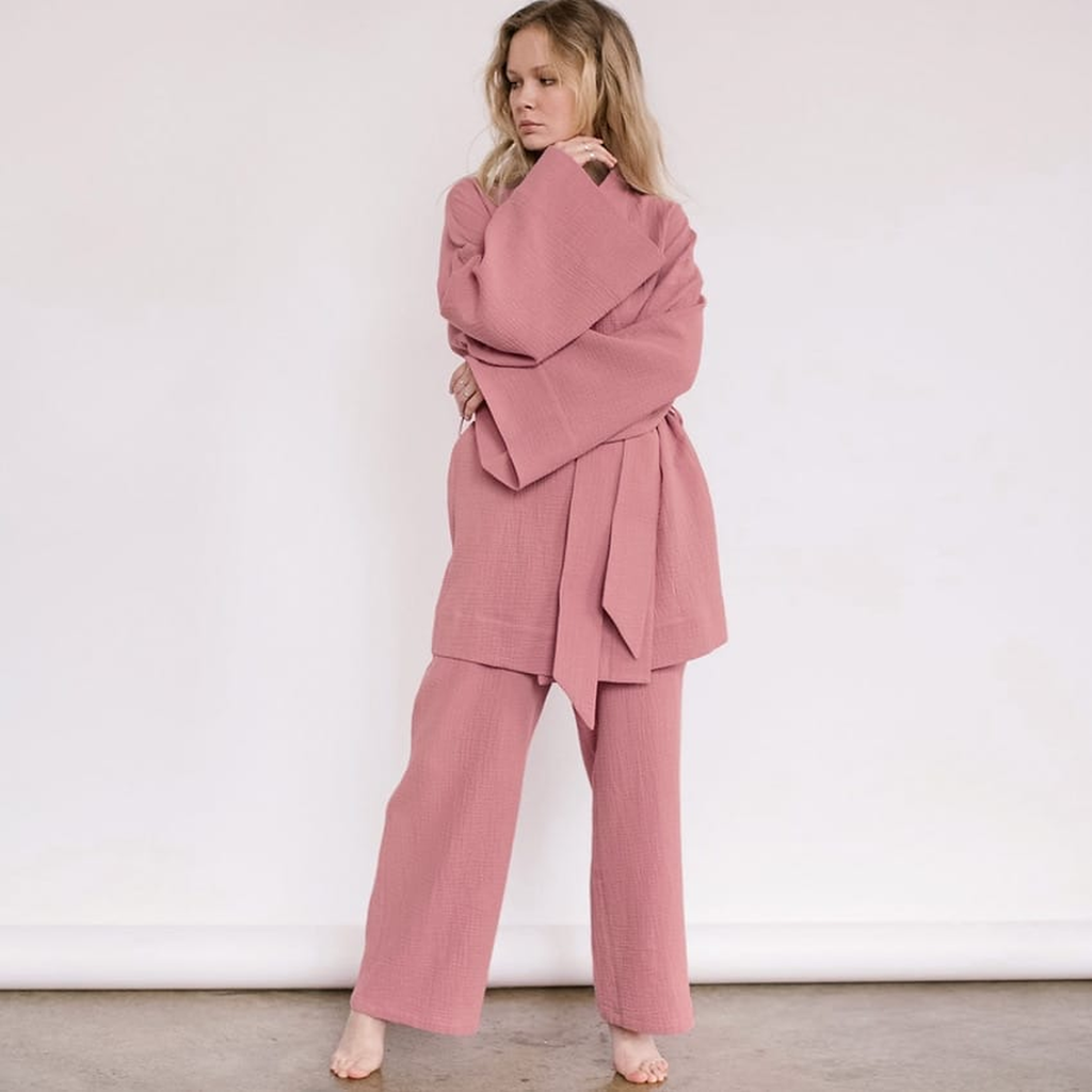 Pyjama kimono rose porté debout, les bras croisés dans les manches larges, ceinture nouée à la taille et pantalon large